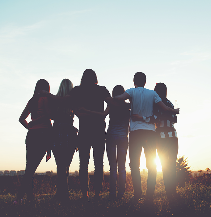 Rear view of two men and four women looking out onto the sun setting onto a field of brush