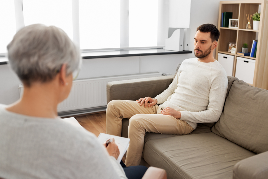 Sullen man undergoing CBT therapy for addiction from older therapist