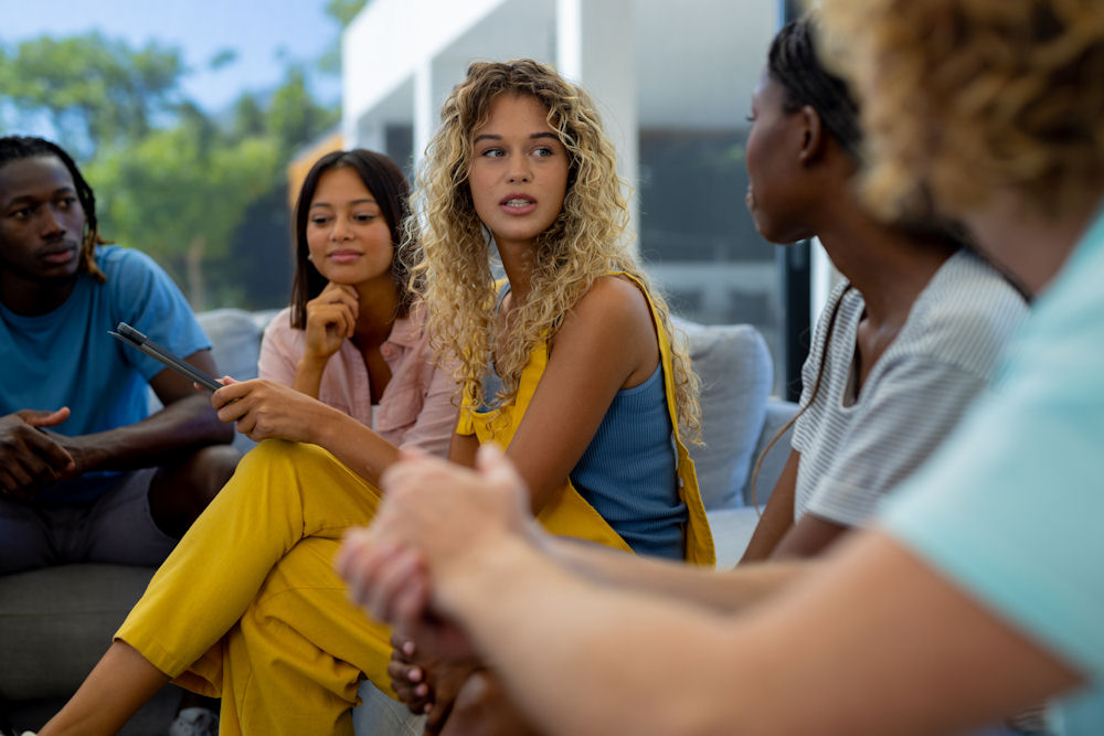 Group of diverse people sitting on sofa, using tablet and talkin Group having a conversation about what triggers their addiction