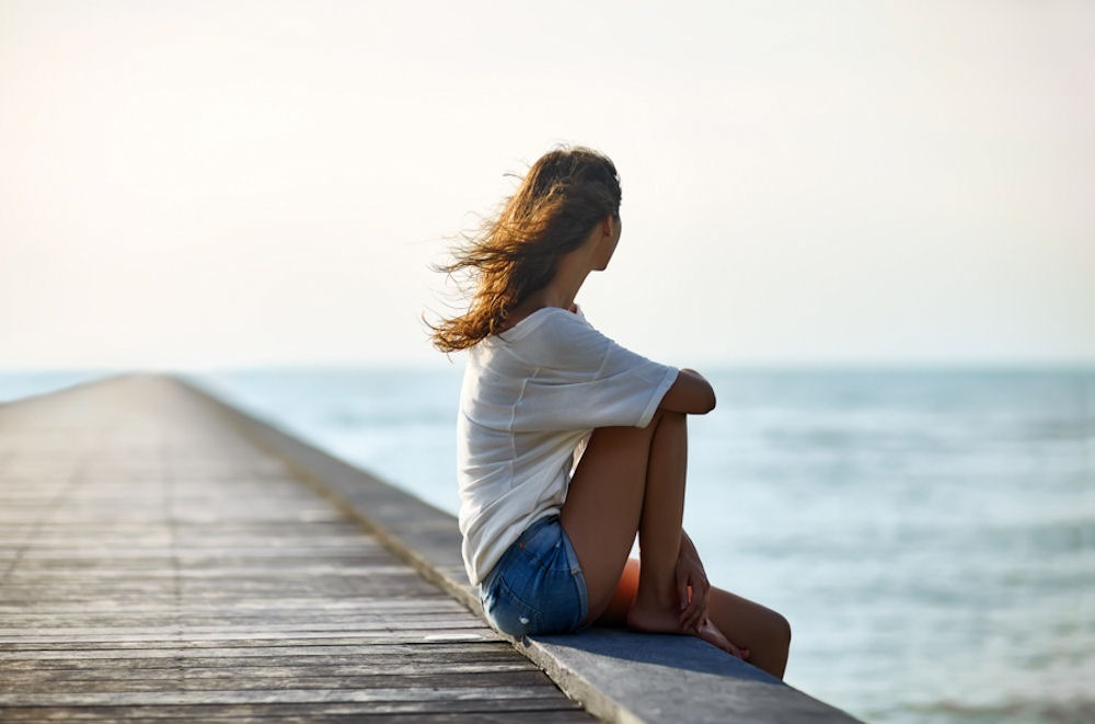 Woman sitting on side edge of dock, looking out at the ocean