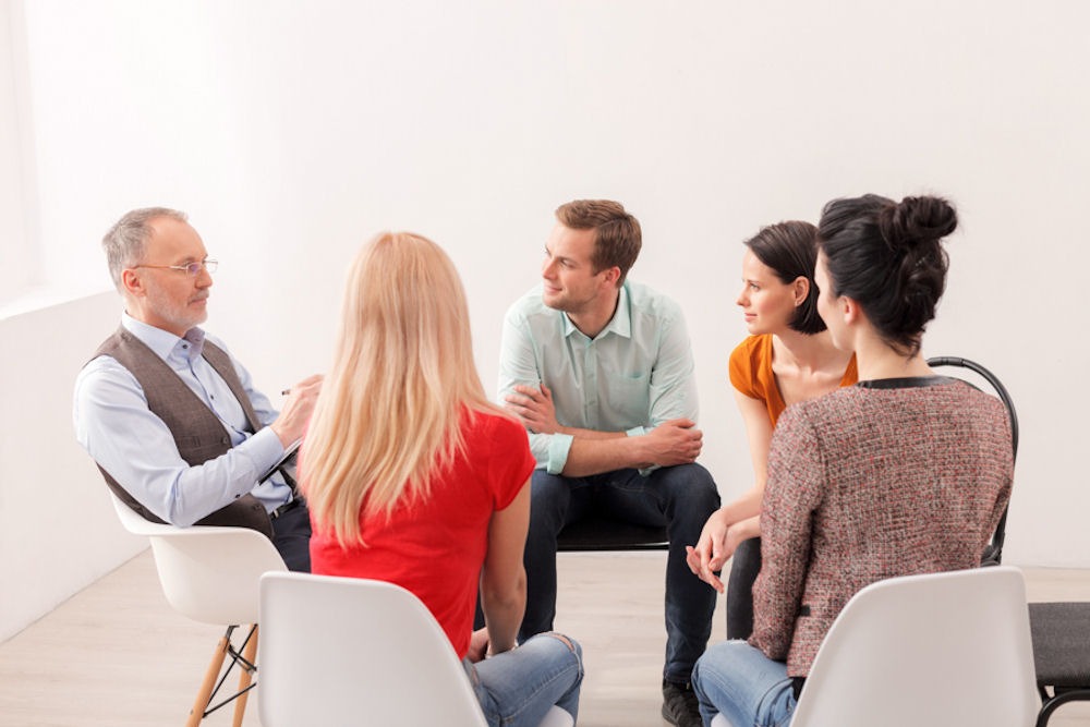 Older male therapist explaining the different types of bipolar disorder to a mixed-gender support group for bipolar