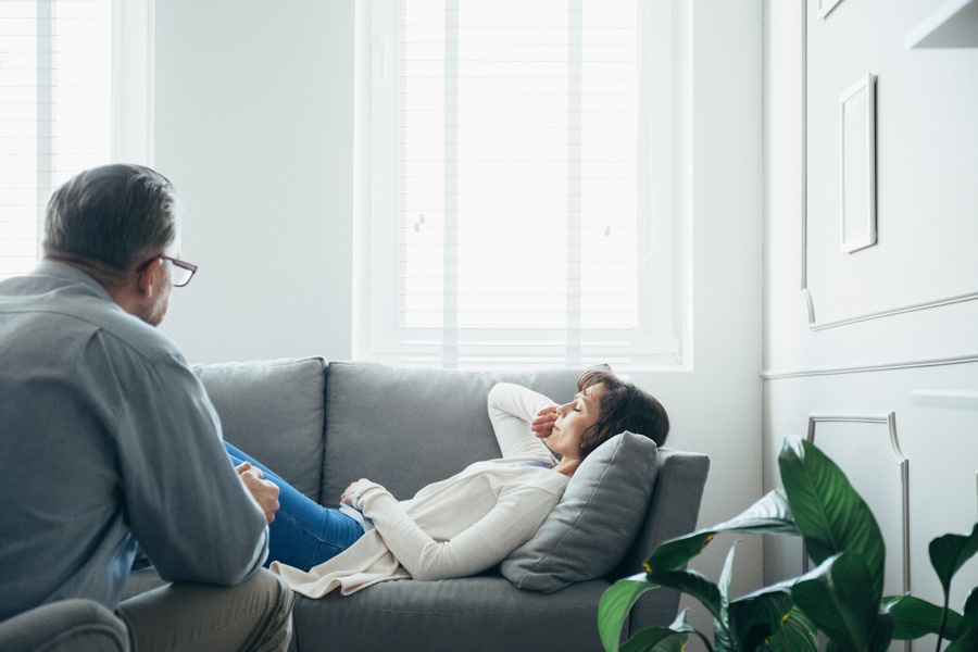 Woman with ADHD and addiction lying on grey couch talking with therapist