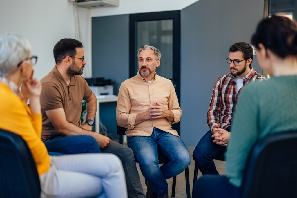 Older man speaking up about trauma and addiction at support group of mostly men