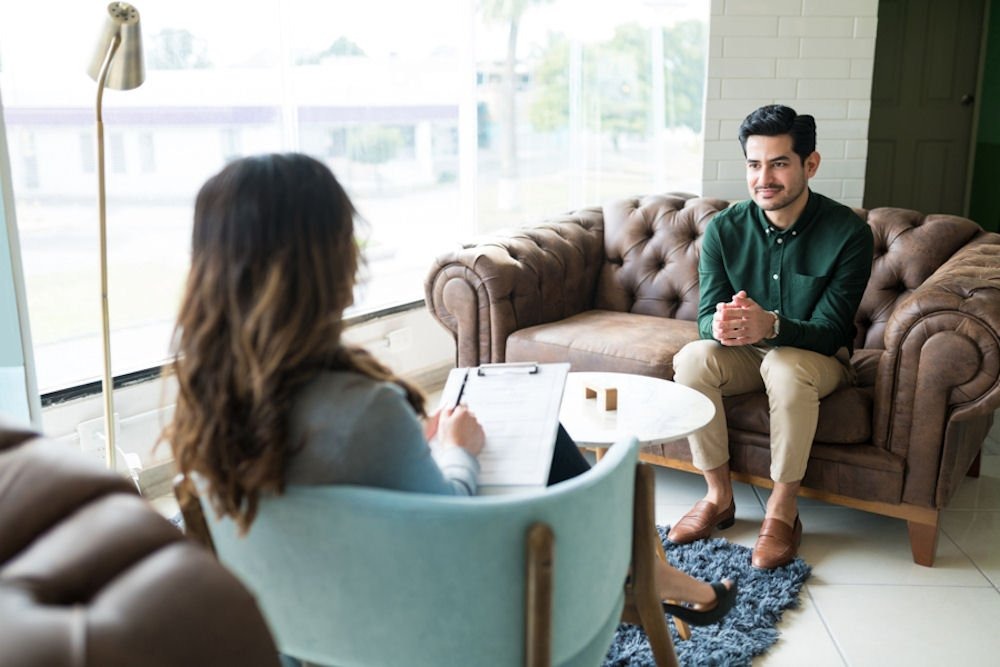 A man and woman are seated on couches in a modern office environment, engaged in conversation