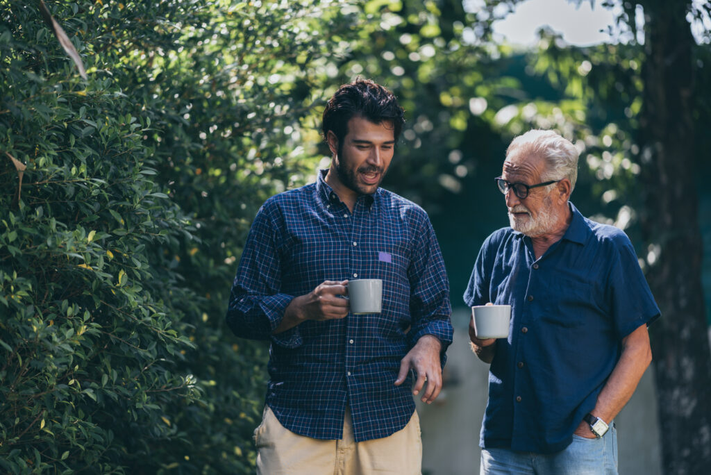 Younger man and older man walking with coffee and discussing who is most likely to become an alcoholic