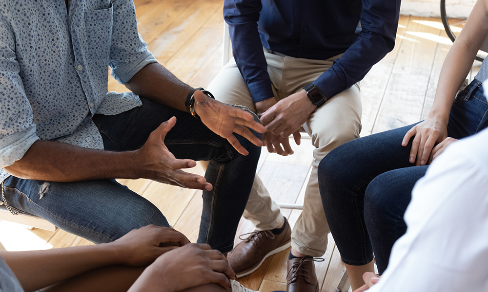 View of hands of support group discussing who is most likely to become an alcoholic