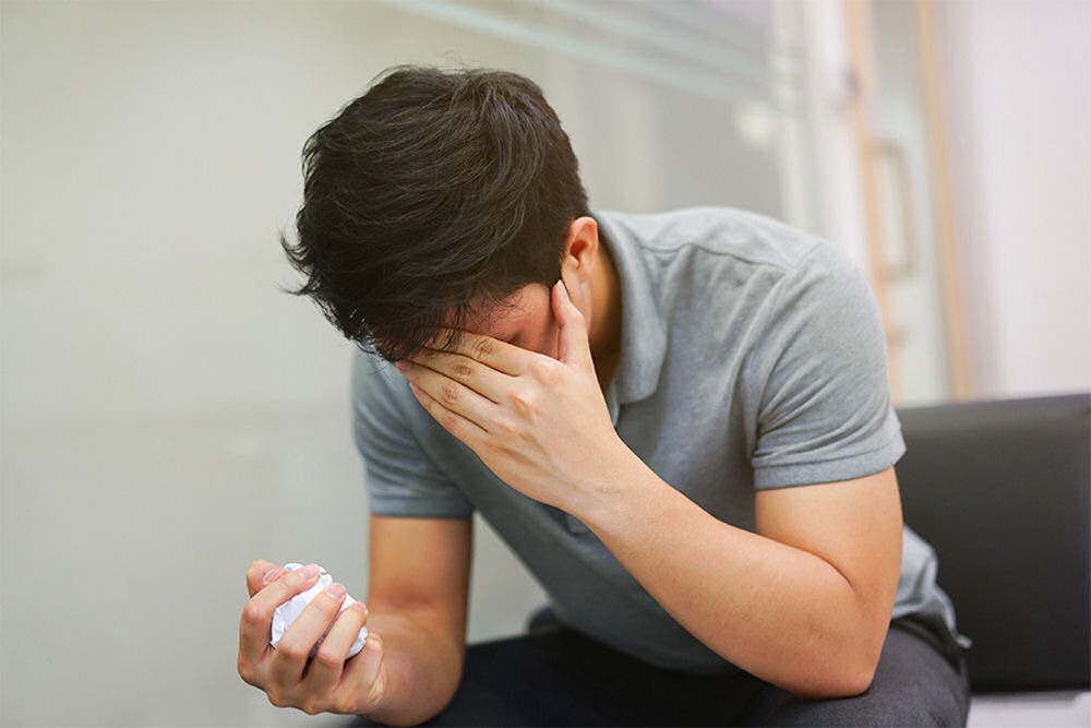 genetics-and-mental-illness-connection man holding head in one hand and crumpled paper in the other hand