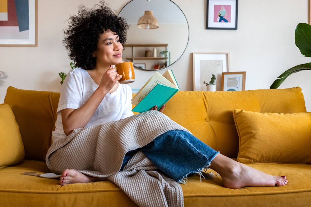 what-to-bring-to-rehab-checklist woman sitting on couch while drinking coffee and reading a book