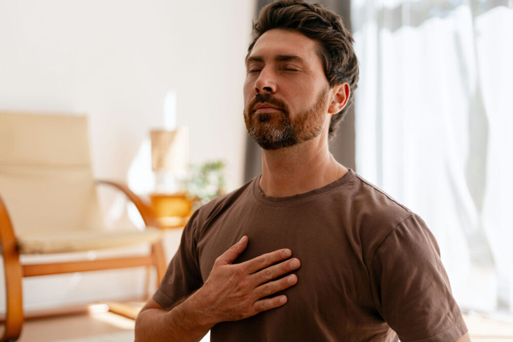 man with eyes closed and hands on his chest to perform breathing exercises and control his anger